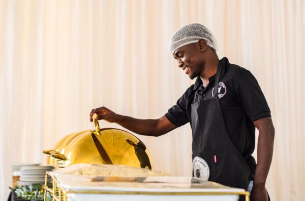 Caterer wearing branded workwear and an apron serving food from a buffet station
